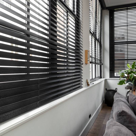 Zwarte houten jaloezieën van JASNO achter en links van de bank